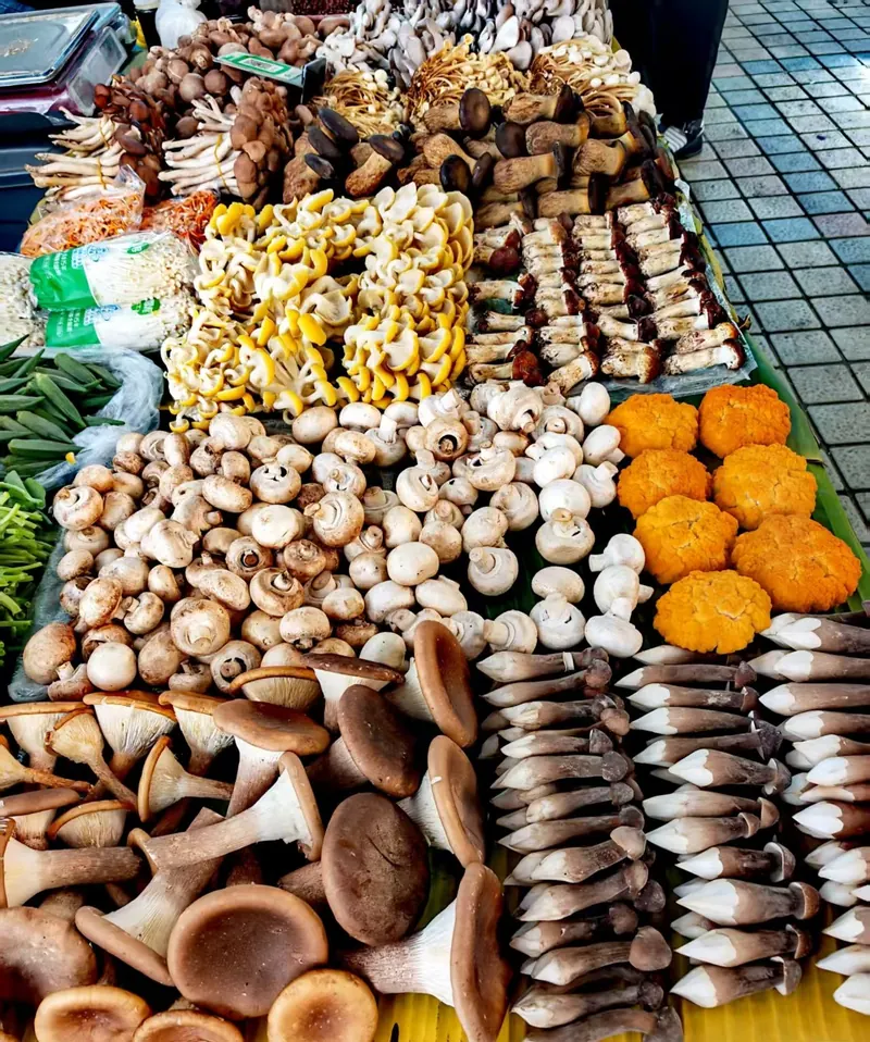 A market stall piled high with wild mushrooms and fresh produce